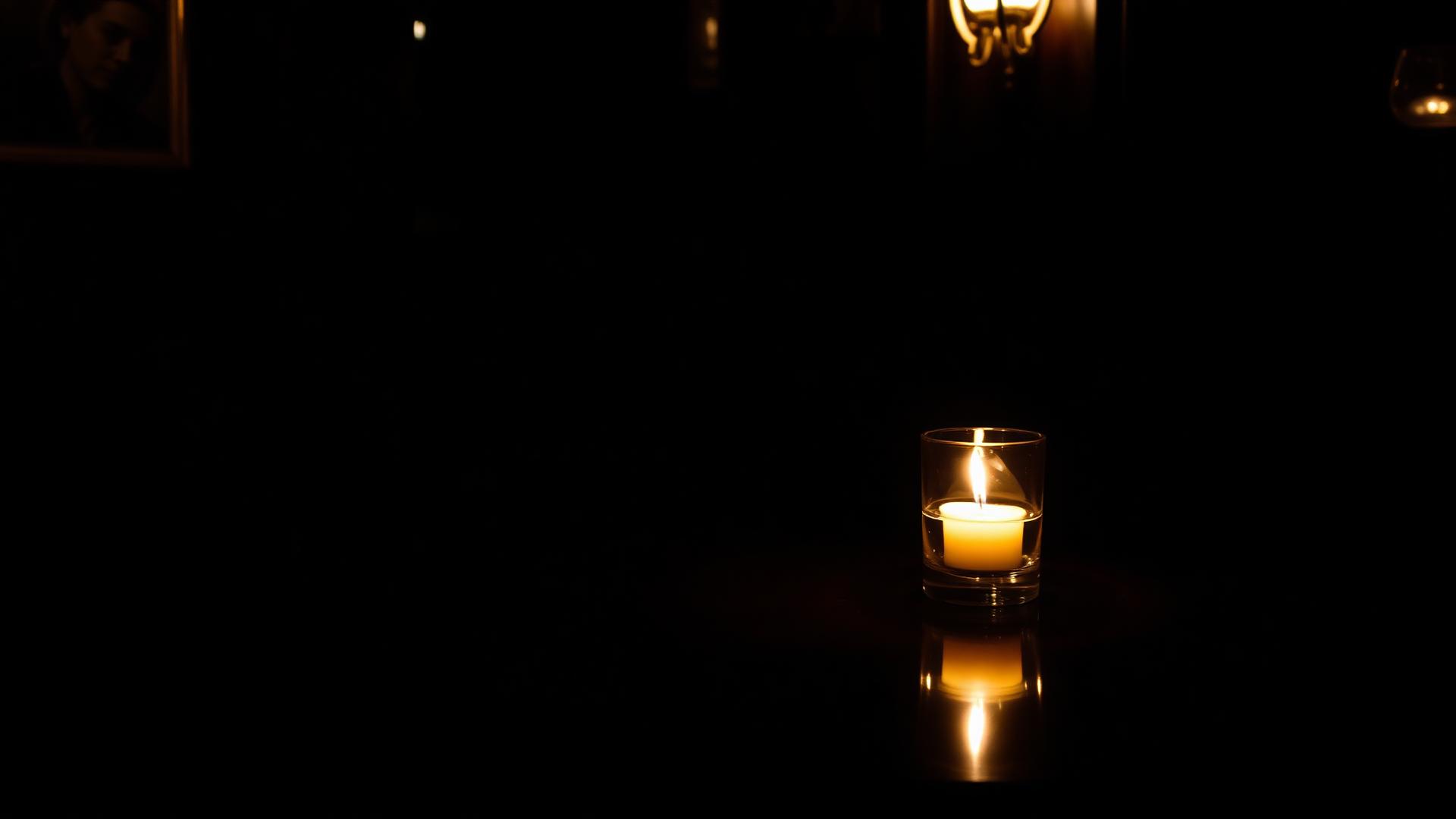 A single candle and a glass on a dark wood table